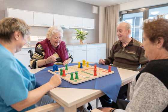Auf Foto spielt eine Pflege-Kraft mit Bewohnern ein Gesellschaftsspiel Auf Foto spielt eine Pflege-Kraft mit Bewohnern ein Gesellschaftsspiel