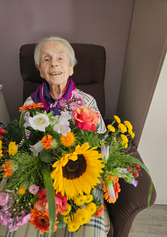 Bewohnerin mit Blumenstrauß sitzt im Sessel