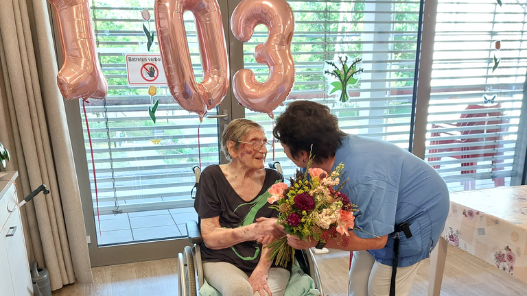 Bewohnerin im Rollstuhl bekommt Blumen von Pflegerin überreicht